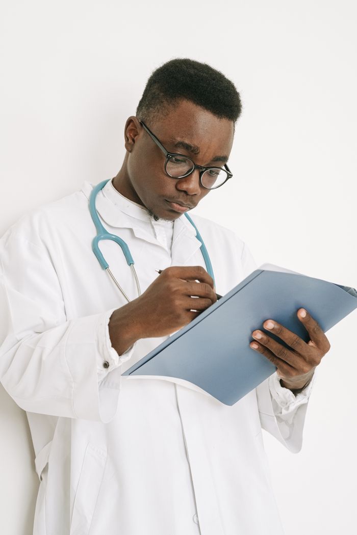 gallery-02 A doctor wearing eyeglasses writes on a medical chart indoors, displaying professional focus.