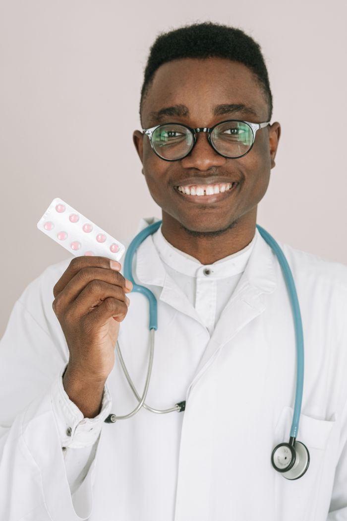 Portrait of a cheerful doctor in a white coat holding a blister pack of pills.