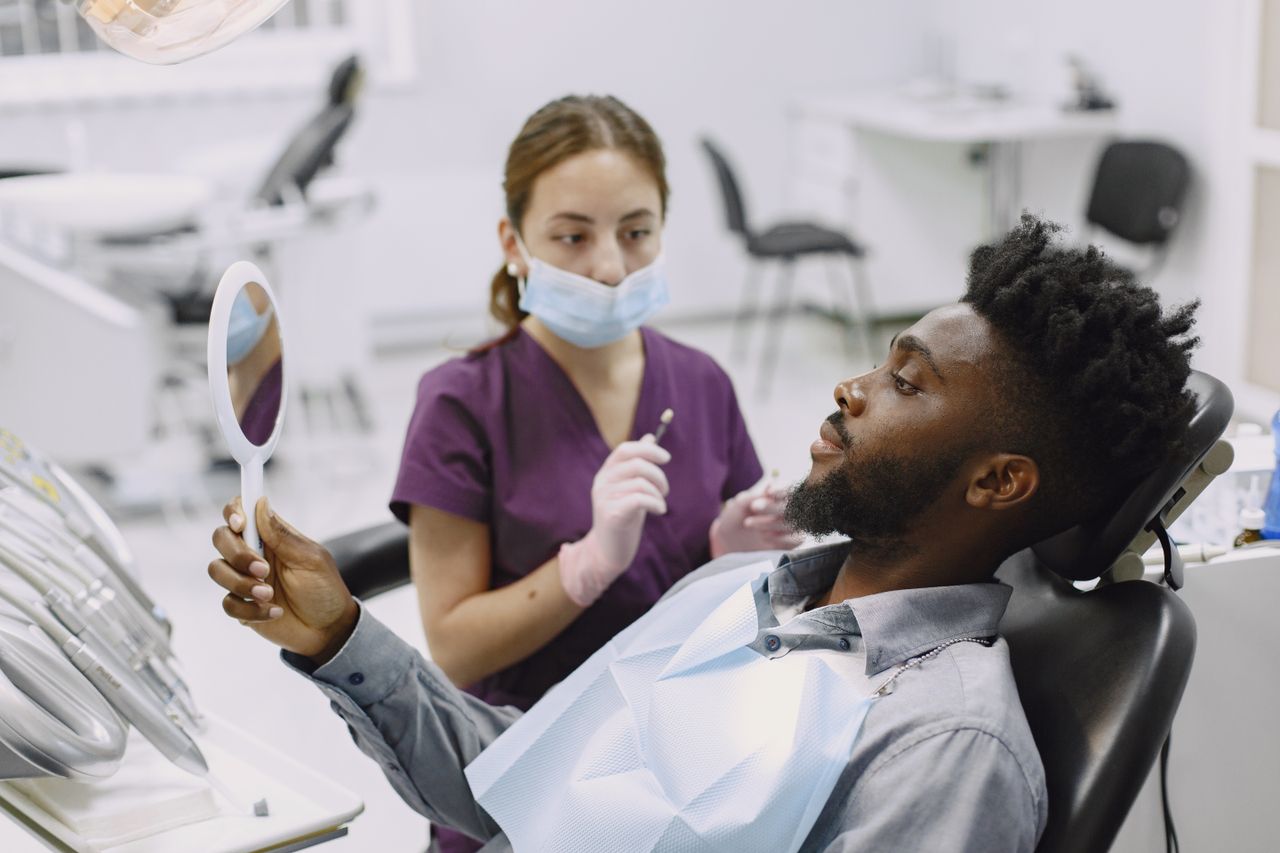 gallery-04 A man in a dental chair during a checkup with a professional dentist using a mirror.